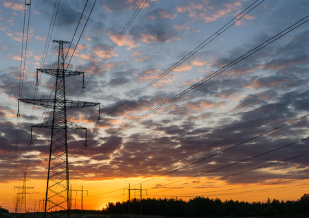 Silhouettes high voltage electric pylon in sunset background.