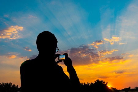 Silhouette of a man photographing the sunset on a smartphoneの写真素材