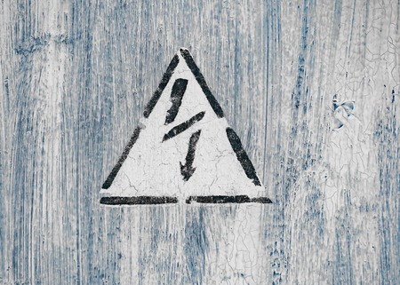 Old risk of electric shock triangle sign on light grey weathered cracked background.の写真素材