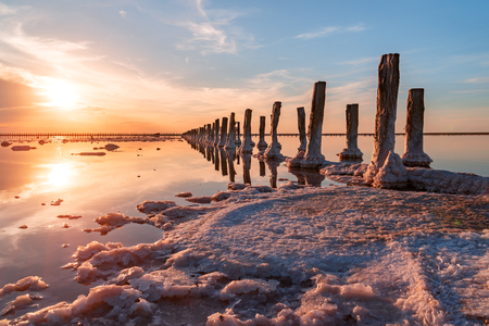 Beautiful sunset or sunrise over a salty lake, Wooden hemp in the build-up of salt after the drying of the lake.の写真素材