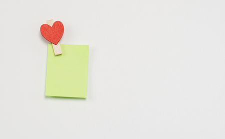 Green paper notes fastened with a wooden clothespin in heart form on a white background.