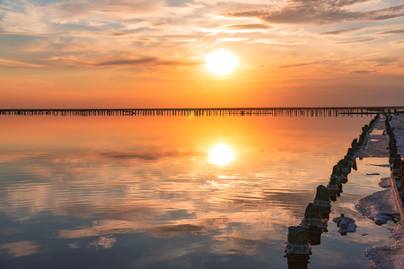 sunset on a pink salt lake, a former mine for the extraction of pink salt. row of wooden pegs overgrown with saltの写真素材