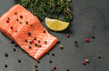 Raw salmon fillet on a dark slate background. Trout fillet with thyme, lime and peppercorns. Wild atlantic fish close up. Healthy food.の写真素材