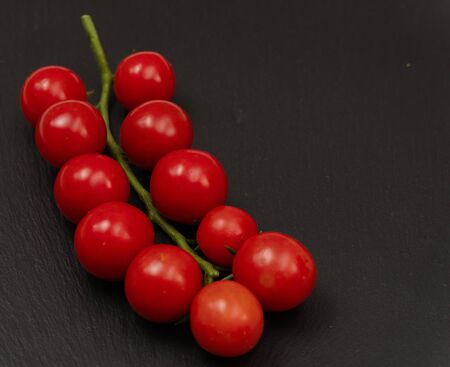 A branch of red cherry tomatoes on a dark slate background. Small and juicy vegetable is rich in vitamins and trace elements. Healthy food. Fresh and organic vegetables. Raw food.の写真素材