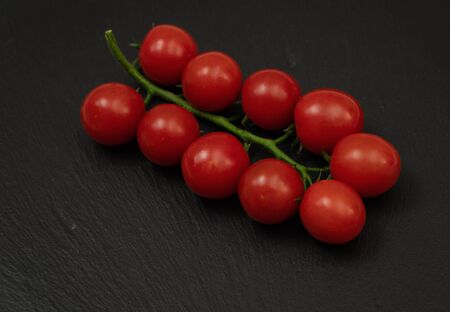 A branch of red cherry tomatoes on a dark slate background. Small and juicy vegetable is rich in vitamins and trace elements. Healthy food. Fresh and organic vegetables. Raw food.の写真素材