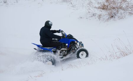 A motorcyclist on an ATV rides off-road in a snowy winter forest.