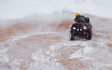 A motorcyclist on an ATV rides off-road in a snowy winter forest.