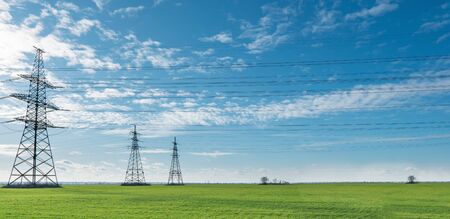 Electrical net of poles on a panorama of blue sky and green meadow.