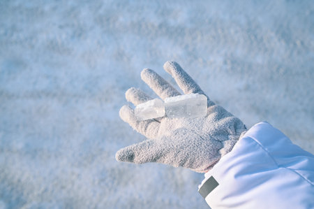 A close-up of a piece of snowy transparent ice on the palm of a hand in a gray glove. Highlighted on a blurry background. A natural invention of nature.の写真素材