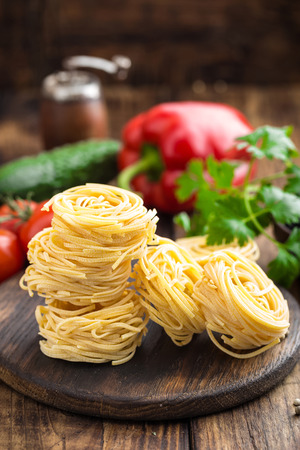 Raw all'uovo pasta, egg noodles with cooking ingredients on dark wooden rustic background, traditional italian cuisineの写真素材