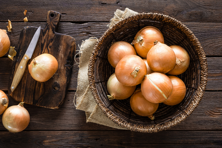 Fresh onion in basket on wooden table, top viewの写真素材