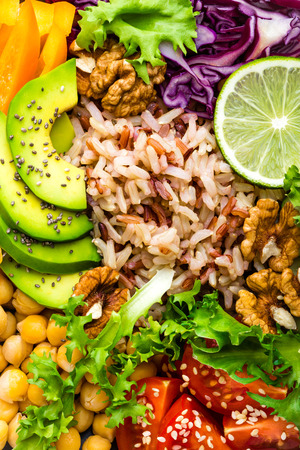 Buddha bowl dish with brown rice, avocado, pepper, tomato, cucumber, red cabbage, chickpea, fresh lettuce salad and walnuts. Healthy vegetarian eating, super food. Top viewの写真素材