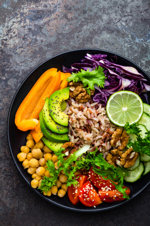 Buddha bowl dish with brown rice, avocado, pepper, tomato, cucumber, red cabbage, chickpea, fresh lettuce salad and walnuts. Healthy vegetarian eating, super food. Top viewの写真素材