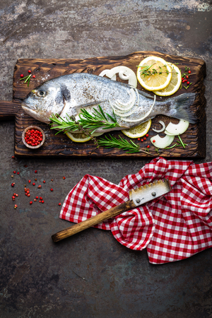 Fresh fish dorado with ingredients for cooking on wooden board. Raw sea bream or dorada fish on dark vintage metal background. Dietary food. Top viewの写真素材