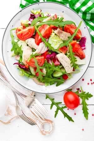 Chicken fillet salad with tomato, lettuce, cucumber and arugula leaves. Fresh vegetable salad with chicken meat. Healthy food. White wooden background. Top viewの写真素材