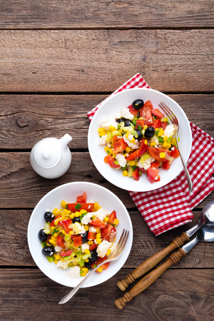 Fresh vegetable salad bowls of tomatoes, corn, pepper, olives, celery, green onion and feta cheese. Healthy food. Diet dinner or lunch menu. Salad plate on table. Flat lay. Top viewの写真素材
