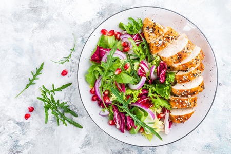 Grilled chicken breast, fillet and fresh vegetable leafy salad with arugula and pomegranate on plateの写真素材