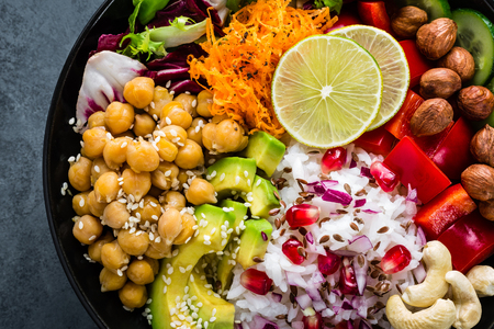 Healthy vegetarian Buddha bowl with fresh vegetable salad, rice, chickpea, avocado, sweet pepper, cucumber, carrot, pomegranate and nuts closeupの写真素材