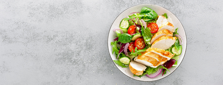 Grilled chicken breast, fillet and fresh vegetable salad of lettuce, arugula, spinach, cucumber and tomato. Healthy lunch menu. Diet food. Top view. Bannerの写真素材