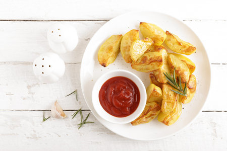 Potato baked and tomato ketchup on white plate, wooden background, top viewの写真素材