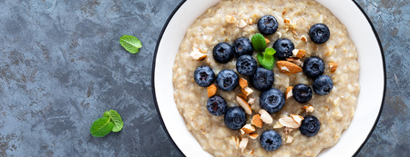 Oatmeal with fresh raw blueberry, almond nuts and honey for breakfast. Healthy vegetarian food. Top view. Bannerの写真素材