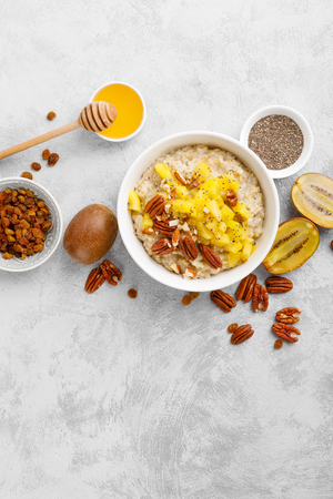 Oatmeal porridge with kiwi fruit, pecan nuts and honey in bowl for breakfastの写真素材