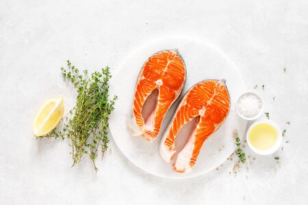 Fresh salmon steaks with ingredients for cooking on white board, view from aboveの写真素材