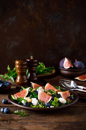 Fig salad with goat cheese, blueberry, walnuts and arugula on wooden background. Healthy food. Lunchの写真素材