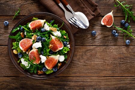 Fig salad with goat cheese, blueberry, walnuts and arugula on wooden background. Healthy food. Top viewの写真素材