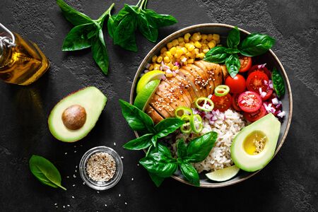 Grilled chicken breast lunch bowl with fresh tomato, avocado, corn, red onion, rice and basilの写真素材
