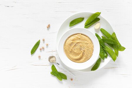 Homemade chickpea hummus served with green peas, healthy vegetarian food concept, top view
