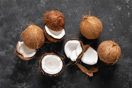 Coconuts cracked and whole on black background, top view