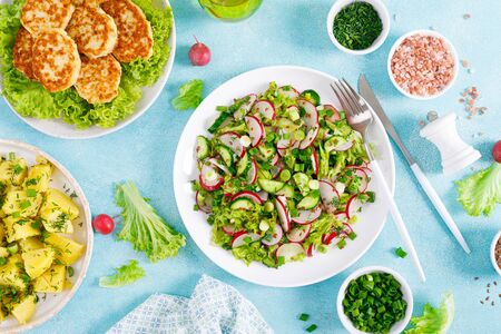 Fresh vegetable salad with radish, lettuce and cucumber, boiled new potato with butter, dill and green onion and fried chicken meat cutlets for lunchの写真素材