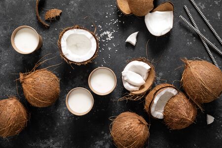 Coconut milk, whole and cracked coconuts on black background, top view