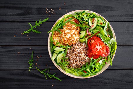 Lunch bowl with buckwheat porridge, fried chicken cutlets and fresh vegetable salad of arugula, lettuce, chard leaves, tomato, cucumber and flax seedsの写真素材