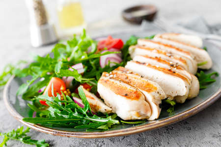 Chicken fillet salad with fresh vegetables and arugula. Fresh vegetable salad of arugula, tomatoes, onion and grilled chicken breast.の写真素材