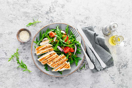 Chicken fillet salad with fresh vegetables and arugula. Fresh vegetable salad of arugula, tomatoes, onion and grilled chicken breast.の写真素材