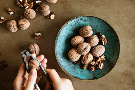 Woman's hands peeling walnuts with a nutcracker on a table, overhead view