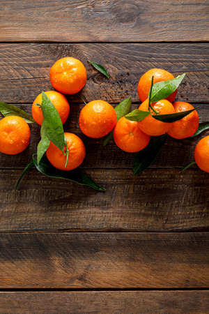 Tangerines, fresh mandarin oranges, clementines with leaves on wooden background. Top view, copy spaceの写真素材