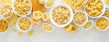 Pasta. Various kinds of uncooked pasta and noodles over stone background, top view with copy space for text. Italian food culinary concept. Collection of different raw pasta on cooking table. Banner.の写真素材