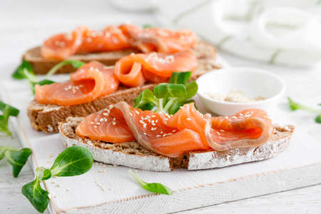 Whole grain rye bread open sandwiches with salted salmon on a white rustic wooden table. Healthy foodの写真素材