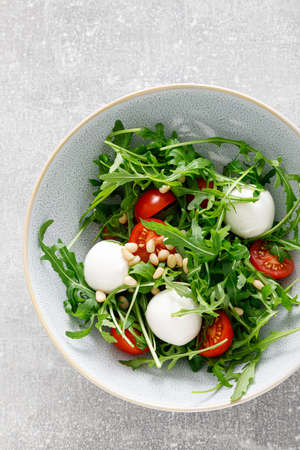 Fresh vegetable Caprese salad with arugula, tomato, pine nuts and mini mozzarella cheese. Top view