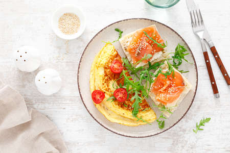 Omelette or omelet, fresh arugula and tomato salad and toasts with butter and salted salmon. Breakfast. Top viewの写真素材