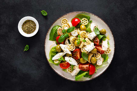 Chicken Caprese pasta salad with mozzarella cheese, olives, tomato and fresh basil. Top view, flat...