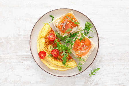Omelette or omelet, fresh arugula and tomato salad and toasts with butter and salted salmon. Breakfast. Top viewの写真素材