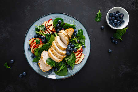 Salad with chicken meat. Fresh fruit salad with chicken breast. Meat salad with chicken fillet, spinach, apples and blueberry on plate, top viewの写真素材