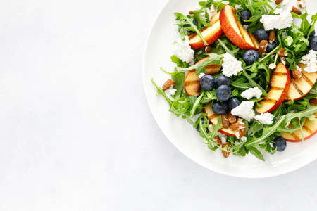Peach, blueberry and arugula fresh fruit salad with cheese and almond nuts, top viewの写真素材