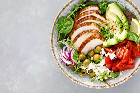 Grilled chicken breast and fresh vegetable salad with tomatoes, feta cheese, olives and avocado. Healthy food. Top viewの写真素材