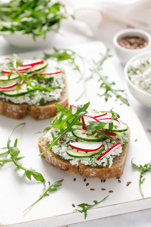 Sandwiches with rye bread toasts, cottage cheese, radish, cucumber, fresh greens and arugula for a healthy breakfastの写真素材