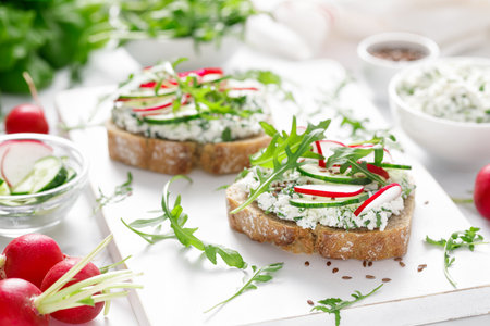 Sandwiches with rye bread toasts, cottage cheese, radish, cucumber, fresh greens and arugula for a healthy breakfastの写真素材